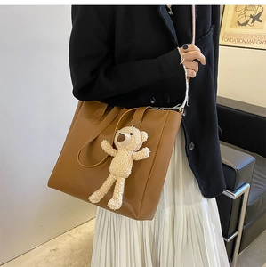 Brown soft leather tote bag with cute plush bear charm worn on shoulder by a model