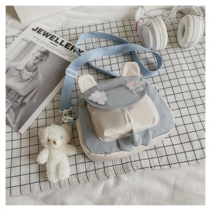 Detail of cartoon bunny ear crossbody bag with plush bear charm and blue fabric strap