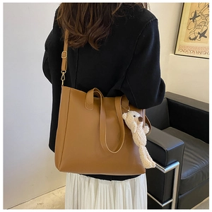 Minimalist caramel brown tote bag with plush bear charm worn by model for commuting