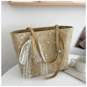Detail of straw woven tote bag featuring floral embroidery and white lace ribbon bow