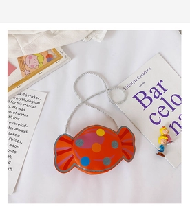 Détail du sac bandoulière orange en forme de bonbon avec pois colorés et bandoulière tressée