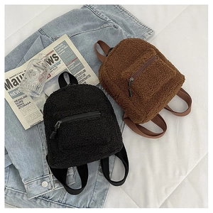 Close-up of black and brown lamb wool mini backpacks on denim jacket background