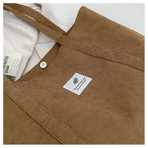 Detail der braunen Cord-Tragetasche mit Stoff-Aufnäher, Textur und magnetischem Verschluss