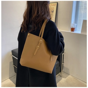 Detailed shot of brown faux leather tote bag with gold buckle on a model shoulder