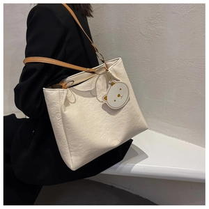 Detail of white embossed tote bag featuring cartoon patterns and teddy bear charm