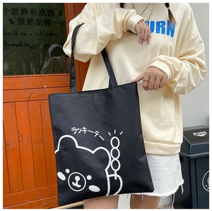 Outdoor shot of black canvas tote bag featuring a white cartoon bear print and Japanese text