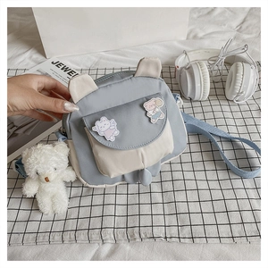 Detail of cute rabbit ear crossbody bag with plush bear charm on soft textile background