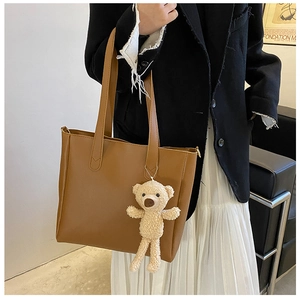 Brown leather tote bag with plush bear charm styled on a model in a black blazer