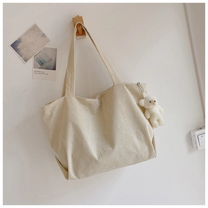 Detailed texture of cream corduroy tote bag with cute plush bear charm on wall