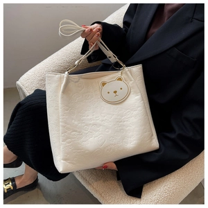 Detail of white embossed leather tote bag with cartoon bear patterns and cute charm
