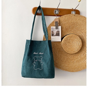 Dettaglio della borsa tote in velluto a coste verde scuro con ricamo orso bianco