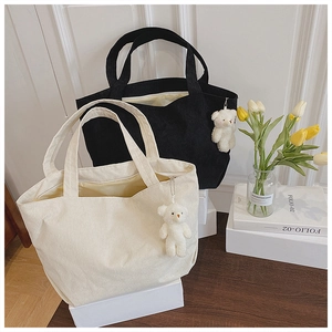 Close-up of corduroy tote bags with plush bear charms on a wooden desk setup
