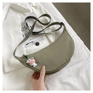 Detail of green crescent canvas bag with cute cow charm and wide strap on white blazer