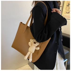 Detailed view of brown PU leather tote bag featuring a cute beige teddy bear pendant charm
