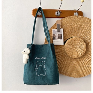 Dettaglio borsa tote in velluto a coste verde con ricamo di orso e ciondolo carino