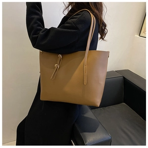 Brown large capacity tote bag with dual straps worn by a model in a black coat