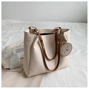 Detail of a creamy white embossed tote bag with cartoon patterns and brown handles