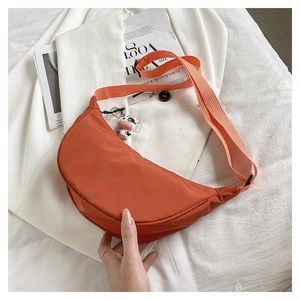 Detail of orange nylon crescent bag with wide strap and cow plush pendant on magazine