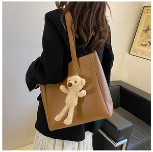 Detailed close-up of brown soft leather tote bag with a plush bear charm on a strap