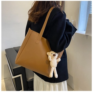Caramel leather tote bag with teddy bear charm shown worn over a black coat