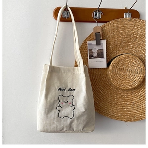 Primo piano di una borsa tote in velluto a coste bianco con ricamo di un orso