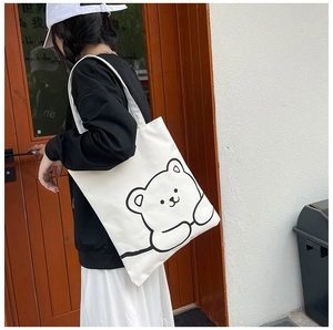 Side view of white canvas tote bag with black cartoon bear print worn on shoulder