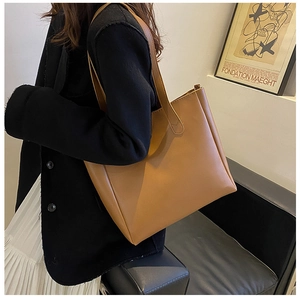 Brown soft leather tote bag worn by model in minimalist home setting, stylish shoulder strap
