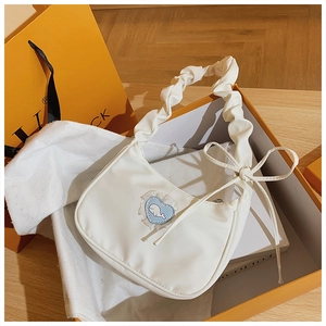 Detail der weißen Plissee-Schultertasche mit Herz-Patch in einer orangefarbenen Box