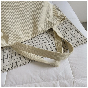 Detail of beige corduroy tote and black white checkered canvas bag set on white surface