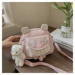 Close-up of pink and white crossbody bag with plush bear charm on a wooden desk