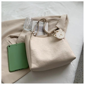 Detail of cream embossed tote bag with cartoon patterns and cat-shaped pendant charm