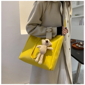 Detail of yellow soft leather tote bag with cute plush bear pendant in cafe setting
