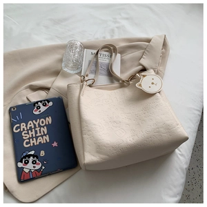 Detail of embossed beige tote bag with bear charm and cartoon pattern on blazer