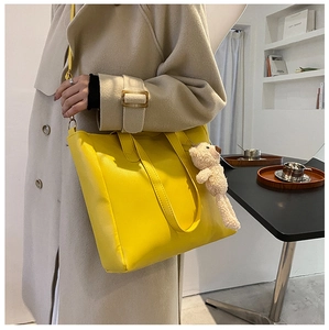 Detail of a bright yellow large capacity tote bag featuring a cute brown plush bear charm