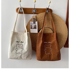 Dettaglio di borse tote in velluto a coste con ricamo di orso in beige e caramello