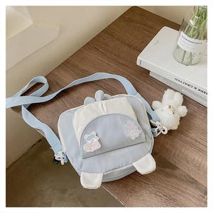 Detail of blue canvas crossbody bag with bunny ears, bear charm on wooden desk