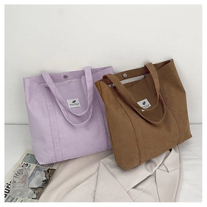 Detail von lila und braunen Cord-Taschen mit breiten Griffen und weißen Stoffetiketten