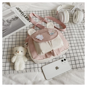 Close-up of pink and white crossbody bag with cute bear ears and plush charm on plaid cloth