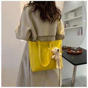 Detailed view of the yellow tote bag worn on shoulder featuring a plush bear pendant