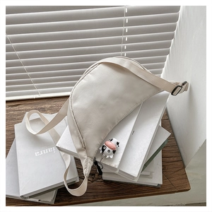 Detail of off-white crescent crossbody bag featuring a cute cow charm and wide strap