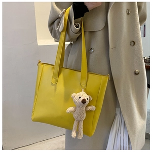Macro view of a bright yellow soft PU leather tote bag featuring a cute teddy bear charm