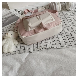 Detail of a pink and white canvas crossbody bag with rabbit ears and bear keychain