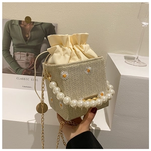 Detailed shot of daisy embroidery, pearl handle and golden chain on a straw bucket bag