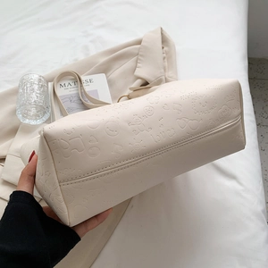 Beige embossed tote bag with cartoon pattern showing bottom stitching and soft leather texture