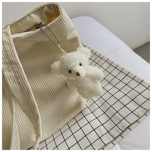 Close-up of cute plush bear charm attached to a cream corduroy tote bag with silver chain