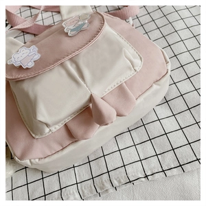Close-up of pink and cream crossbody bag with cute bear badges on checkered fabric
