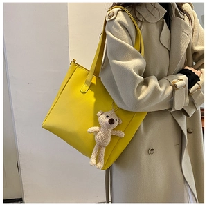Detail of a bright yellow tote bag with a cute plush bear charm on a beige wool coat