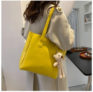 Detail of yellow faux leather tote bag featuring a cute teddy bear charm and side zipper
