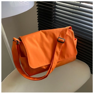 Detail of bright orange oxford crossbody bag with black adjustable strap on white chair