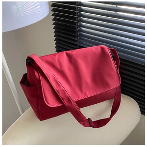 Detail view of red nylon crossbody bag with flap closure and adjustable strap on a chair